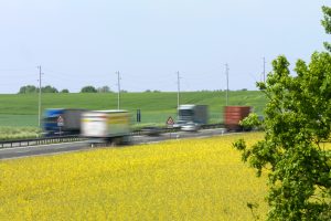 Umweltschutz: Blühendes Rapsfeld mit Lkw auf einer Autobahn im Hintergrund
