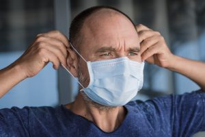 Mann trägt Gesichts-Einweg-Maske als Virenschutz, Mit Maske gegen die Pandemie
