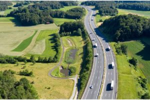 Autobahn zeigt Pkw- und Lkw-Verkehr auf einer Autobahn in Vogelperspektive, eingerahmt von grünen Bäumen und Wiesen